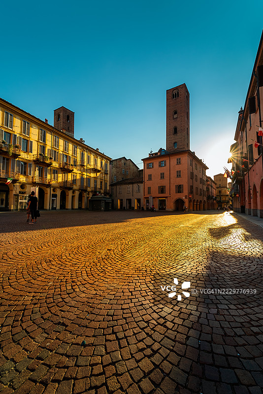 意大利阿尔巴的阳光照耀的鹅卵石广场与中世纪塔楼图片素材