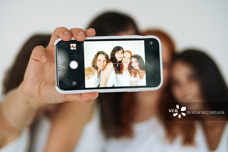 一群多样化的年轻女性在白色背景下用智能手机自拍图片素材