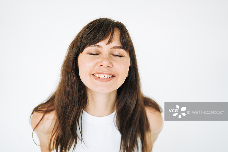 年轻的棕发女性模特闭着眼睛，简约风格的白色背景肖像图片素材