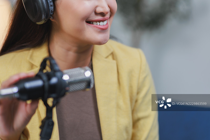 亚洲演讲者佩戴耳机录制播客，面带微笑图片素材