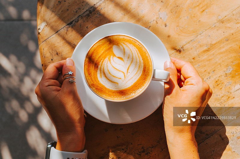 女性手中拿着早晨的卡布奇诺，阳光下的俯视图图片素材