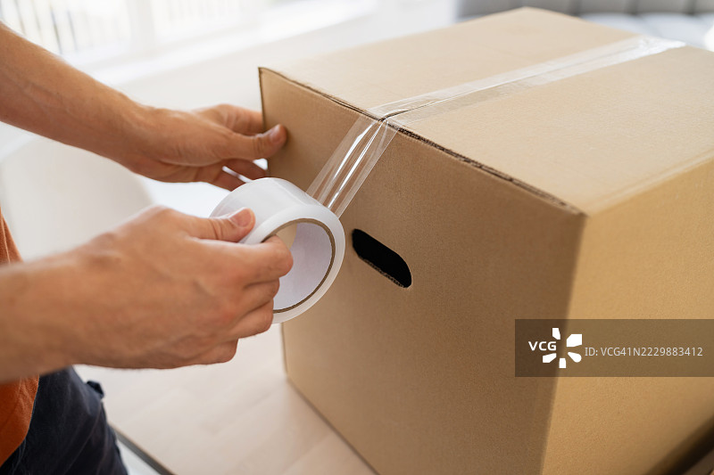 一个人在打包运输的纸箱上贴胶带图片素材
