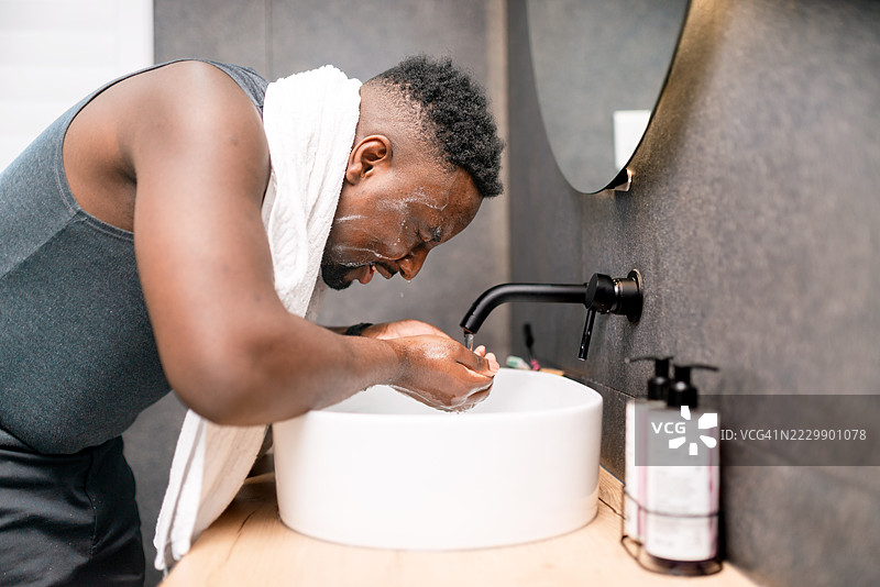早晨例行公事中，男子在浴室用毛巾围住脖子洗脸图片素材