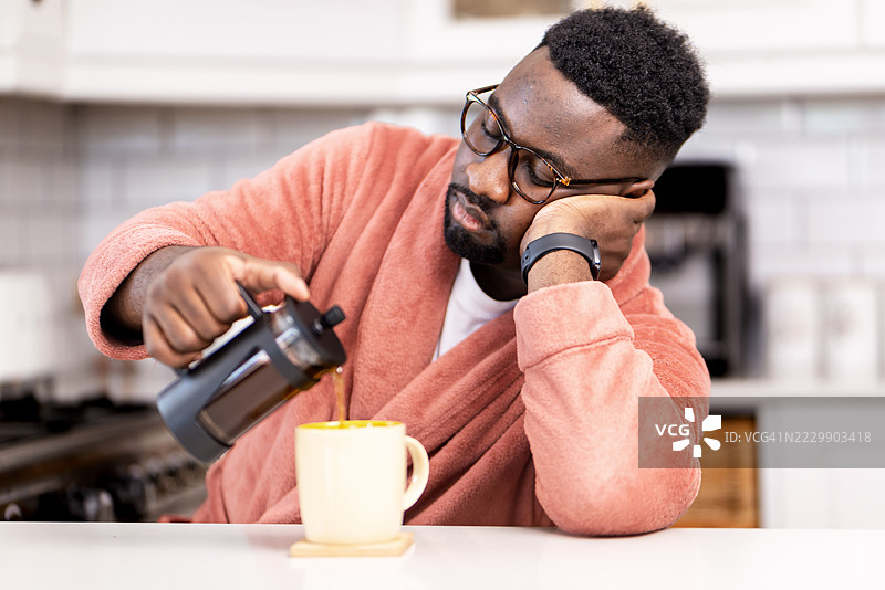 男人在早晨的厨房里倒咖啡，感到困倦图片素材