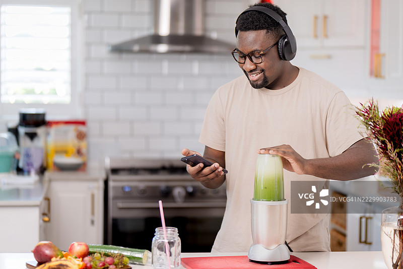 男子在现代厨房里一边听音乐一边准备绿色果昔图片素材