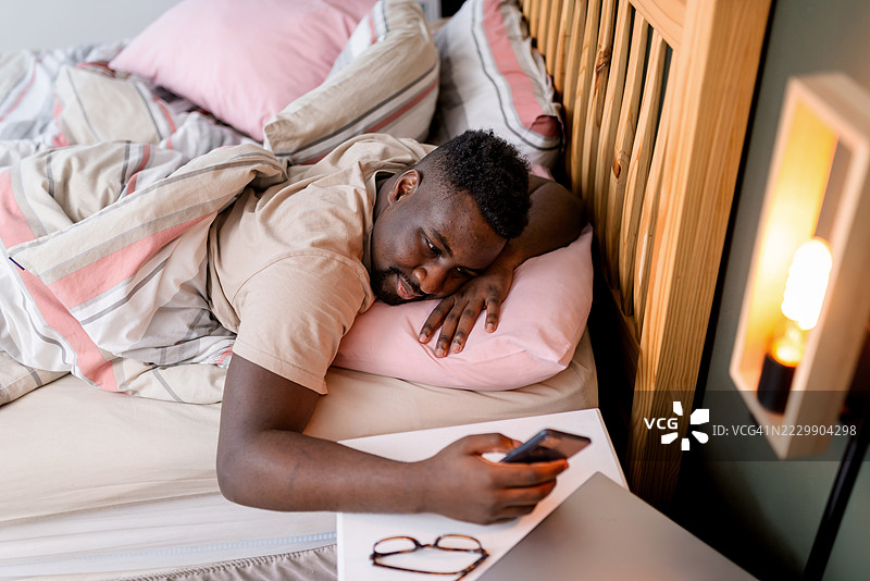 男人在早晨的床上放松，使用智能手机图片素材