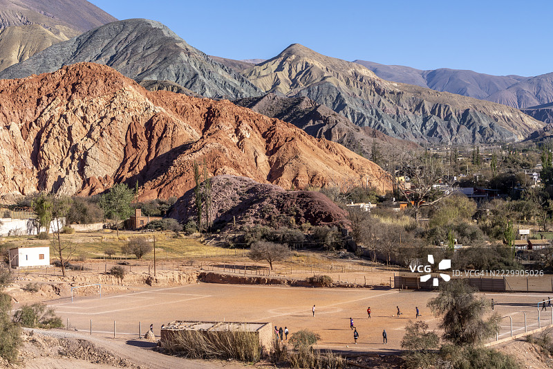 年轻人在阿根廷胡胡伊省普尔马马克玩足球，背景是五彩斑斓的山丘和侵蚀景观。图片素材