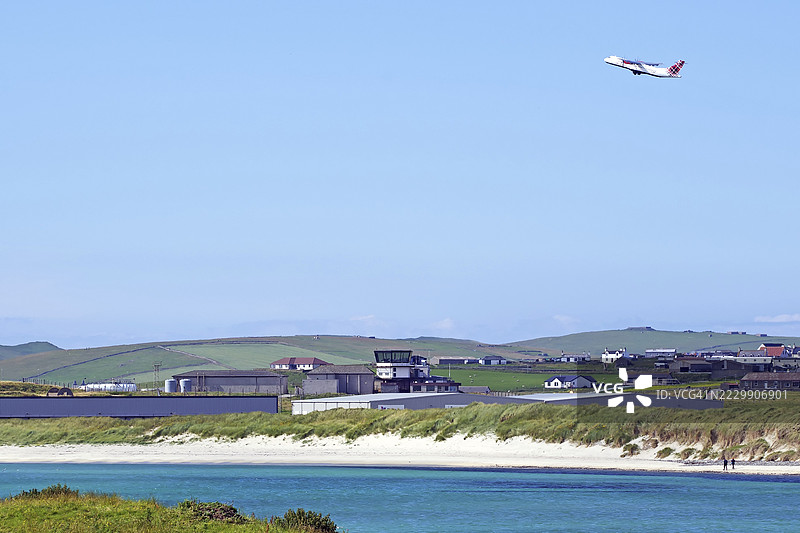 飞机在苏姆堡角(Sumburgh Head),设得兰群岛(Shetland Islands),英国(United Kingdom)上空起飞,背景是海岸、机库和绿色土地。图片素材