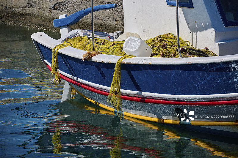 一艘蓝色渔船和渔网停靠在阿纳利普西、马尔特扎纳、阿斯提帕利亚、德德卡尼斯群岛的港口水面上，希腊。图片素材