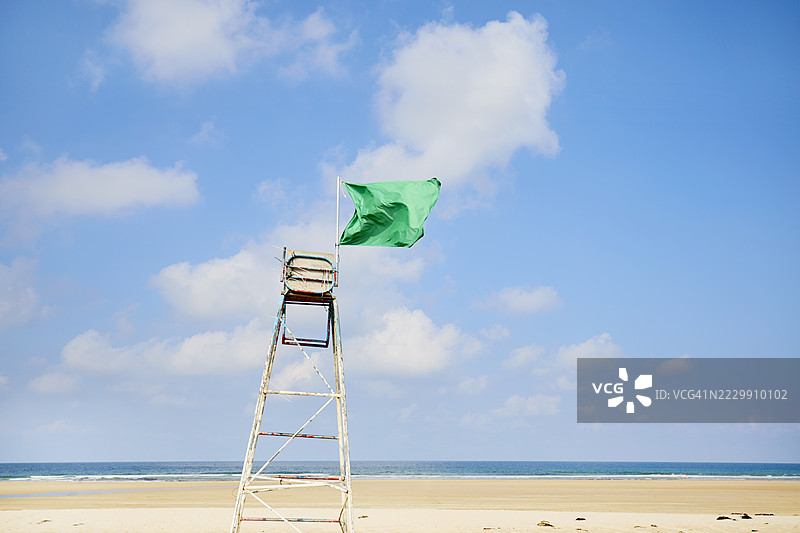 在蓝天和白云下，救生椅旁的绿色旗帜在风中飘扬图片素材