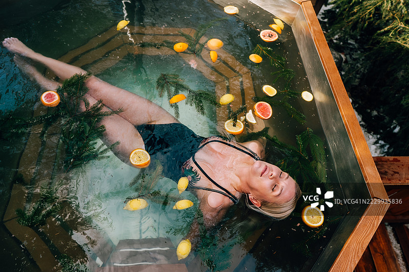 女人在热水浴缸中放松，周围有柑橘水果和松枝，俯视图图片素材