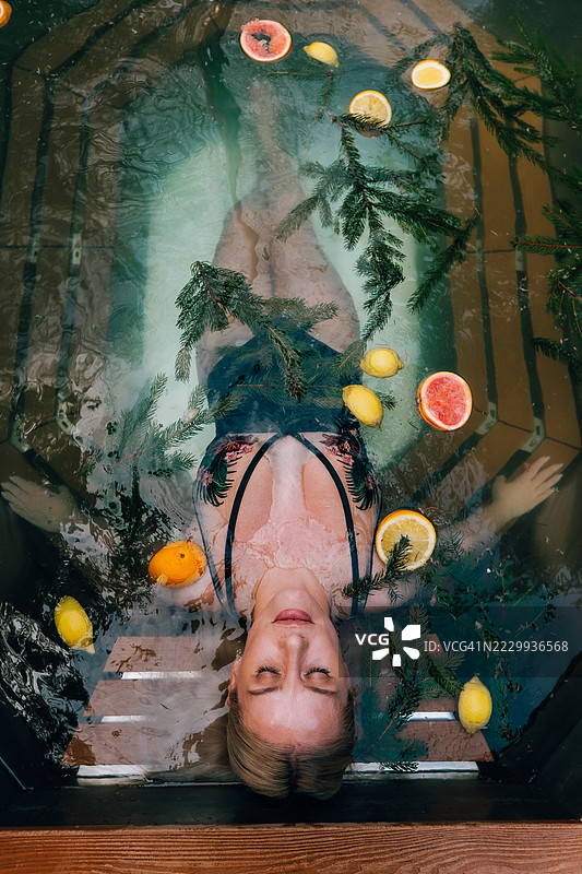 美丽的女性在水疗中心放松，周围有柑橘水果和松枝，俯视图图片素材