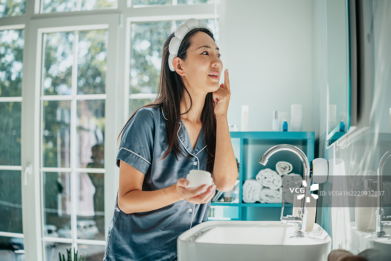 一位快乐的亚洲女性在明亮的浴室中进行早晨护肤程序图片素材