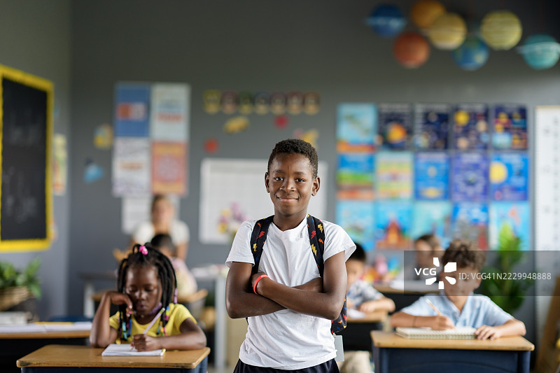 自信的学生站在教室里，背景中有同学们。图片素材