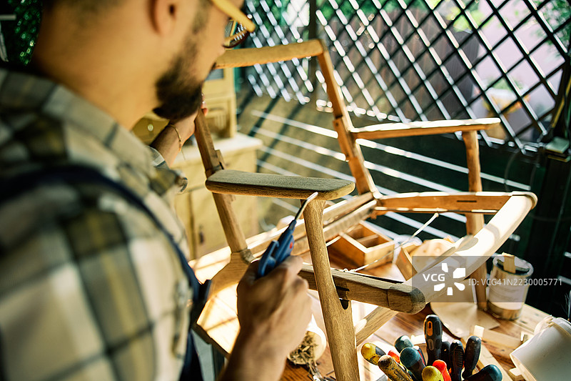 男子在家中的工作坊里修复木椅，白天时光。图片素材