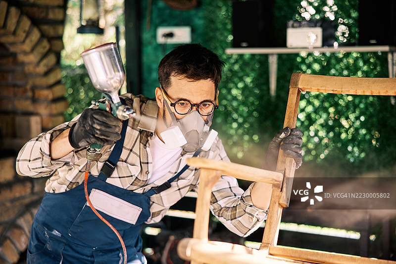 工匠穿着防护装备在工作坊里给木椅上漆图片素材