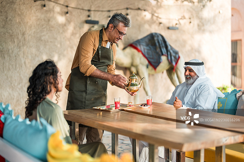 中东男性咖啡馆老板在户外为多样化顾客提供饮品图片素材