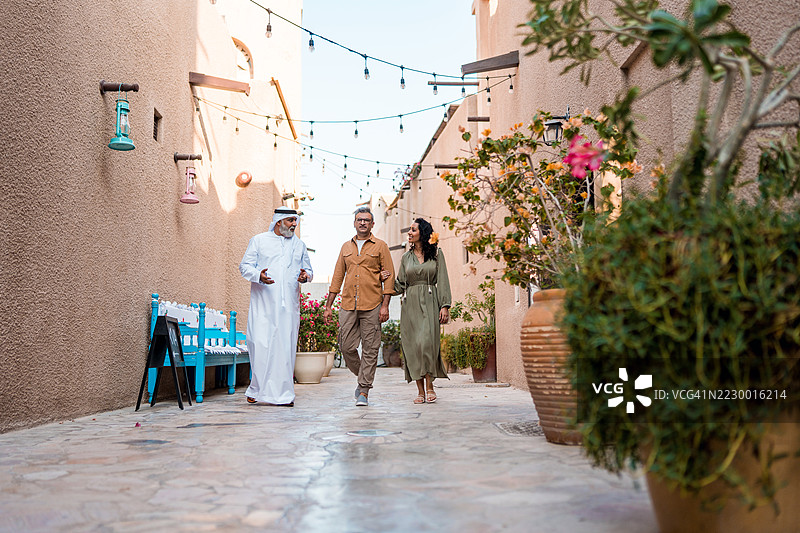 友好的导游带领情侣穿过迷人的迪拜小巷，那里挂满了串灯和传统装饰。图片素材