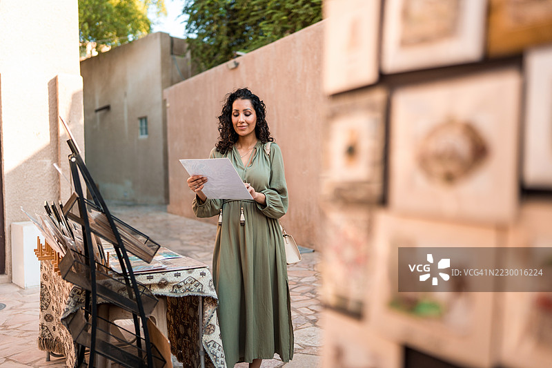 中年阿拉伯女性在传统的阿尔法希迪区购物，穿着绿色连衣裙图片素材