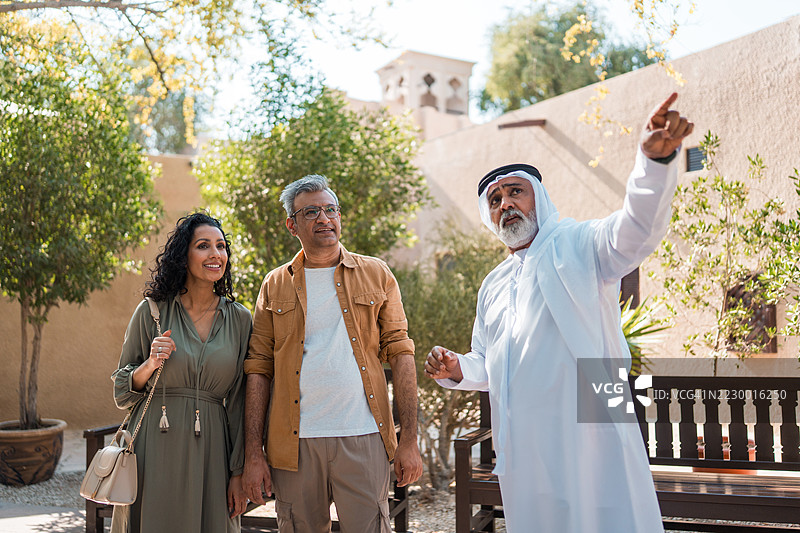 资深阿拉伯导游带领中年阿拉伯夫妇在历史悠久的旧迪拜户外游览，阳光明媚。图片素材
