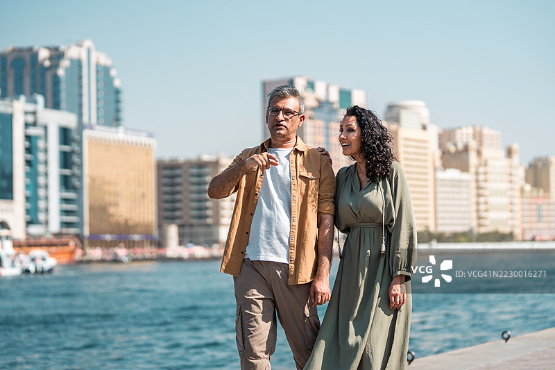 中年阿拉伯夫妇在迪拜滨水区漫步，背景是迷人的城市天际线图片素材