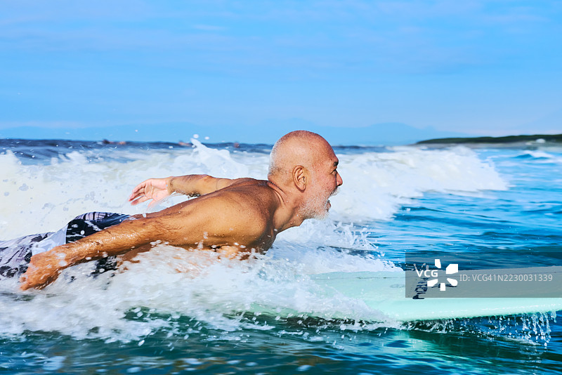 老年冲浪者在太平洋的海浪中划水冲浪板图片素材