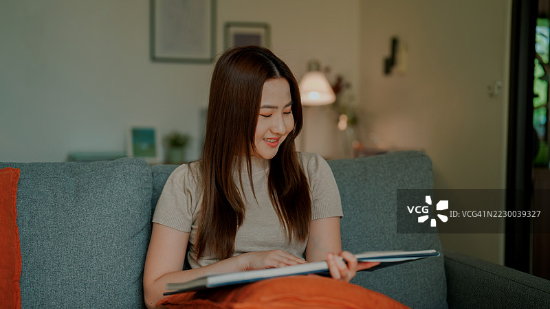 年轻的亚洲女性在家中安静地阅读书籍，享受放松时光。图片素材