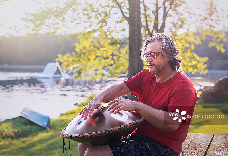 一位白发苍苍的男士在波科诺湖边演奏手碟鼓。图片素材