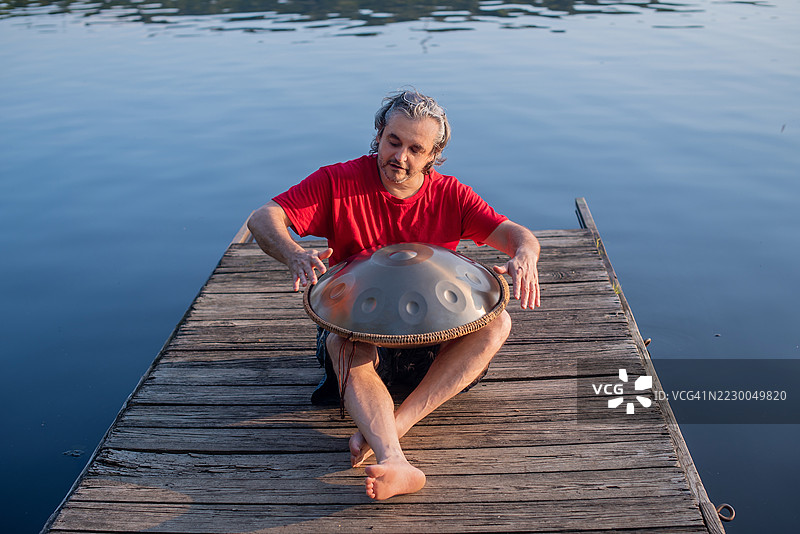 一位爱好者在木码头上创作音乐。一位54岁的业余爱好者在宾夕法尼亚州波科诺湖边演奏手碟乐器。图片素材