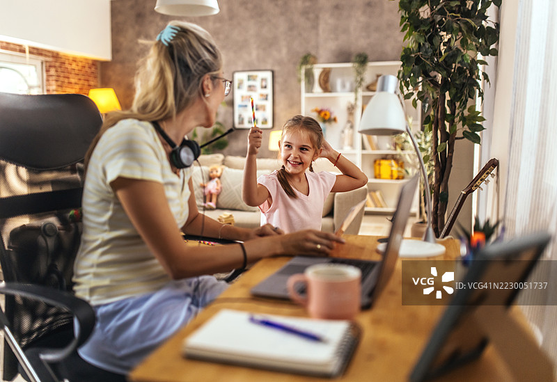 在家工作，妈妈专注于她的工作，而她的孩子在客厅玩耍。图片素材