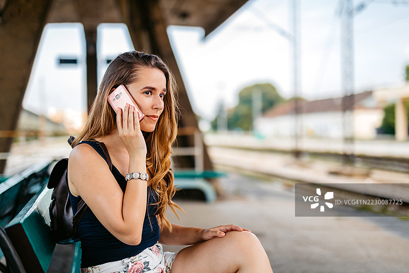 年轻女性坐在火车站的长椅上打电话图片素材