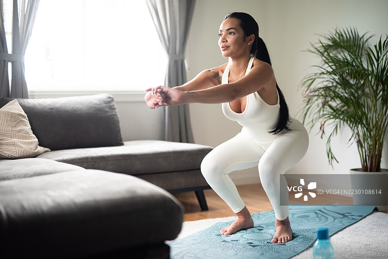 穿着运动服的棕发女性正在做乌鸦式或椅子瑜伽姿势。图片素材