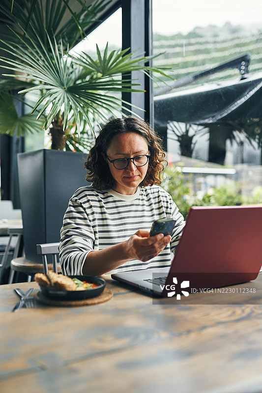在明亮的咖啡馆环境中使用笔记本电脑和智能手机的女性图片素材