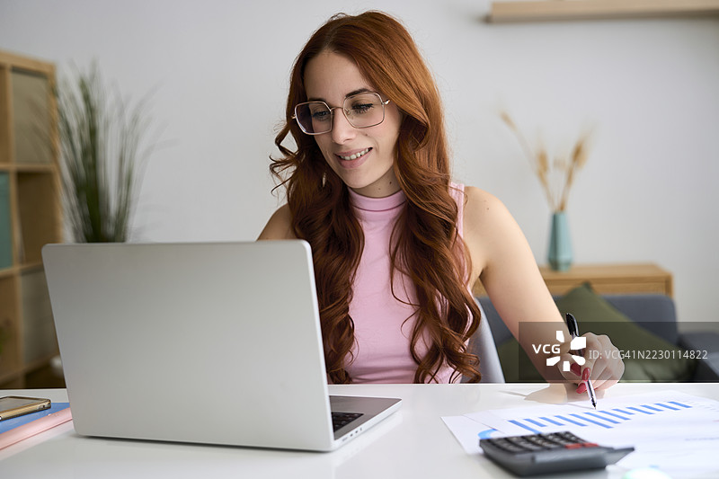 年轻女商人在家办公室分析图表并使用笔记本电脑工作图片素材