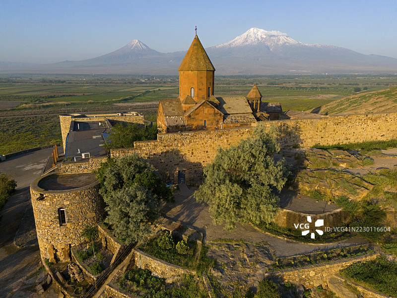 土耳其阿拉拉特省，一座具有历史意义的教堂，拥有石砌墙壁，坐落于蓝天映衬的山景前，俯瞰着亚美尼亚的霍尔维拉普修道院，其背景是阿拉拉特山和小阿拉拉特山，并提及了深邃的地牢。图片素材