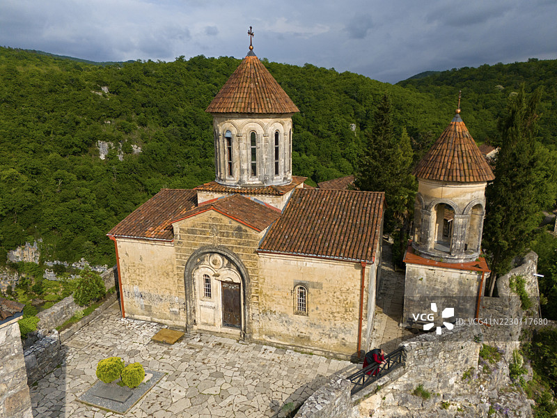 俯瞰格鲁吉亚伊梅列季大区库塔伊西附近的莫特萨梅塔修道院，近景是铺着瓷砖屋顶和石墙的教堂，背后是树木繁茂的山丘。图片素材