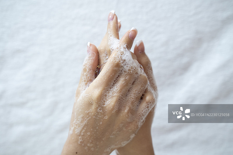 美丽的女性手部，手中有肥皂、护肤乳液或洗涤泡沫，背景为灰米色。图片素材