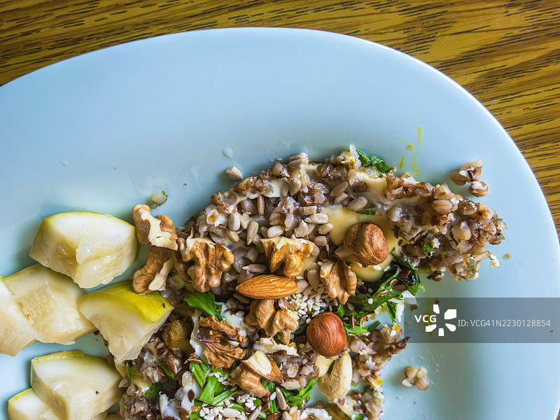 木板上放着荞麦粥，上面放有切片梨、混合坚果、种子和散落的新鲜香草，呈现出乡村风格的健康早餐。图片素材