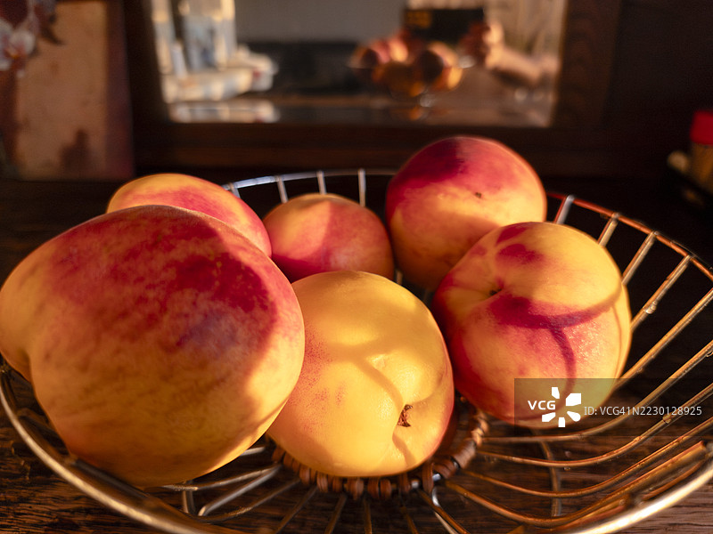 阳光下成熟的桃子安静地躺在复古金属篮子里，散发着温暖和夏日的清新，背景柔和的金色让人感受到乡村厨房的魅力。图片素材