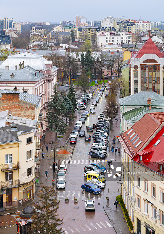 雨天的城市风景，展示了停放在伊万诺-弗兰基夫斯克街道旁的车辆，行人在阴云密布的天气中穿行于湿滑的人行道旁的城市建筑。图片素材