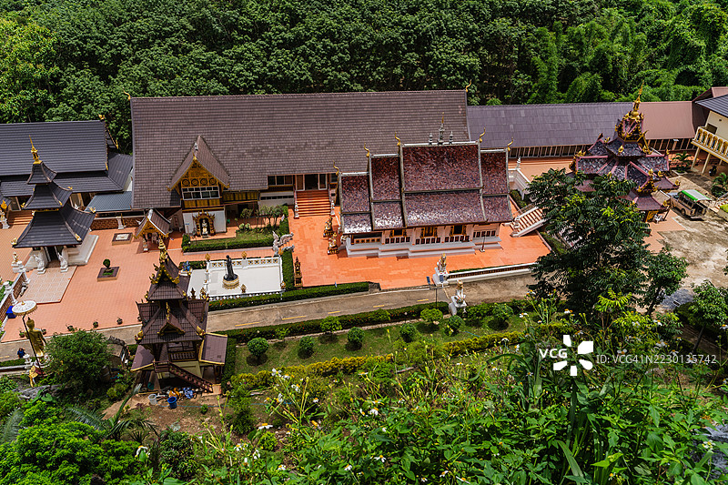 从山顶的视角可以看到一个广阔的泰国寺庙群，金色的佛塔和华丽的建筑被茂密的绿色森林环绕。图片素材