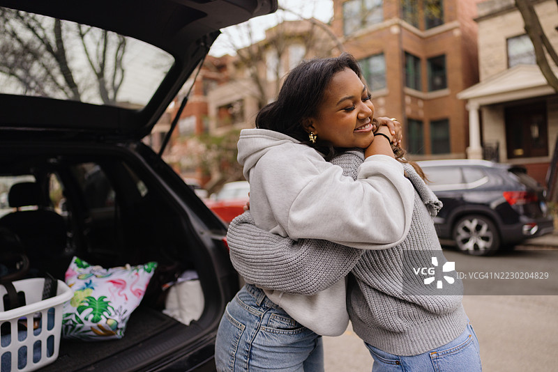 两个年轻女性在一辆后备箱打开的汽车旁拥抱。图片素材