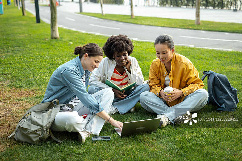 大学朋友们在户外一起学习，围坐在一台笔记本电脑旁。图片素材