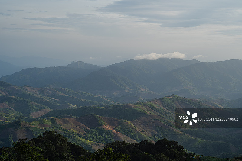 广阔的山脉和山谷在多云的天空下延展，阳光的斑驳照亮了有纹理的地形。图片素材