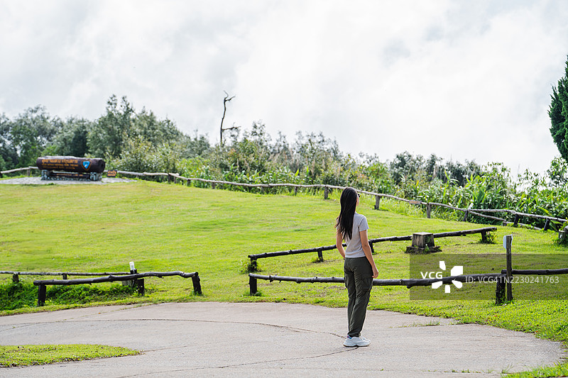 一位穿着休闲服的女性站在铺砌的山间小道上，四周环绕着郁郁葱葱的绿树，俯瞰着云雾缭绕、宁静的背景。图片素材