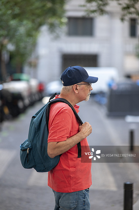 城市街道上，背着背包的老年男子侧面轮廓，穿着红色 polo 衫。图片素材