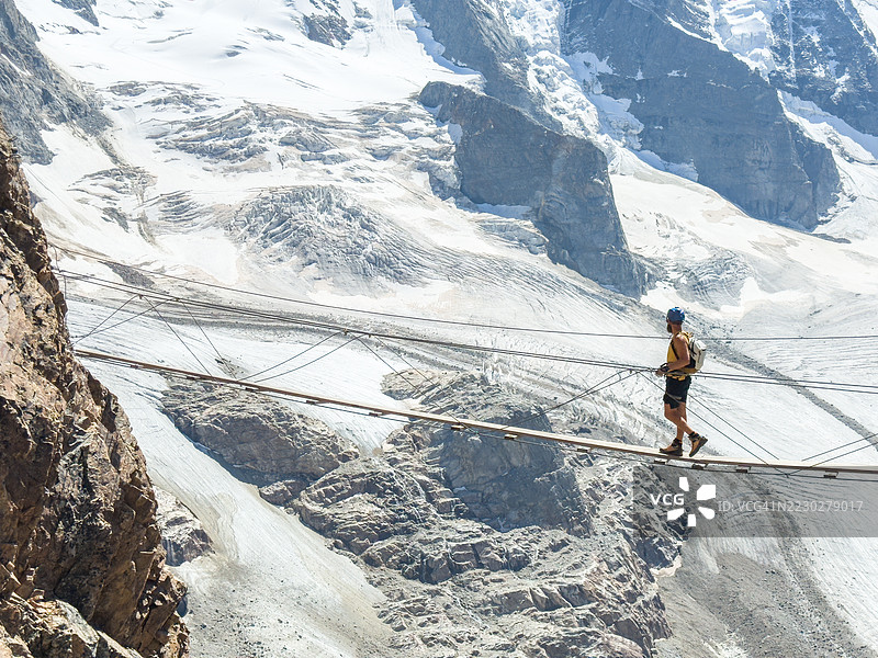 男子穿越悬索桥，背景是山间冰川图片素材