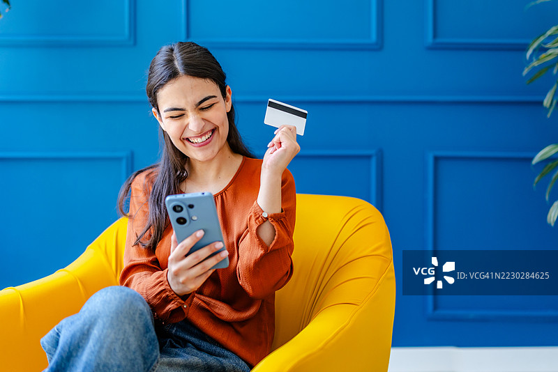 年轻女性在舒适的客厅里坐在明亮的黄色椅子上享受网上购物。图片素材