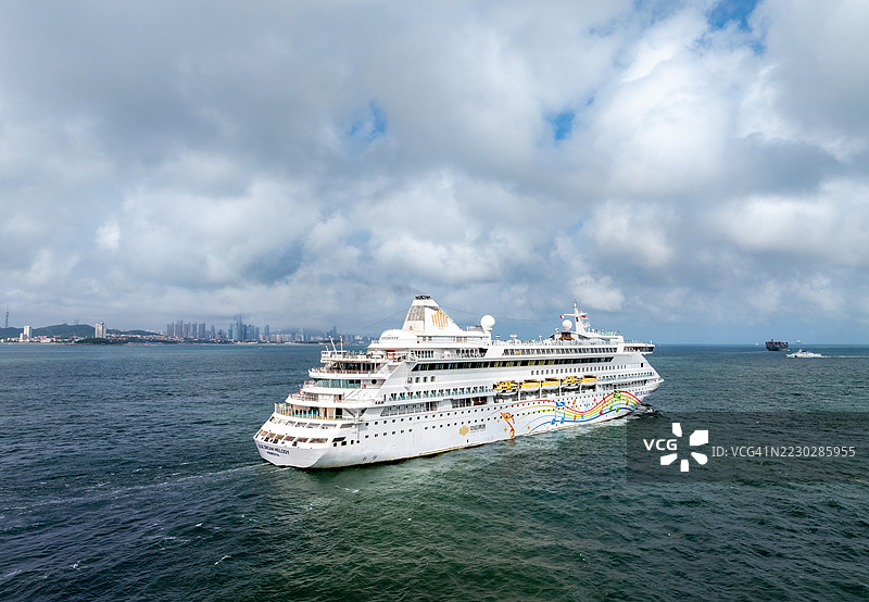 无人机视角下的蓝梦旋律号客轮在海上航行，背景是青岛市天际线。青岛市，位于中国东部的山东省。图片素材