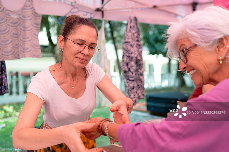 在露天市场摊位上，摊主正在给顾客戴手链。图片素材